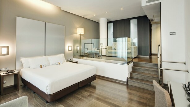 A modern hotel room with a large bed, bedside tables, a mirror, and a staircase leading to an upper level. - Hotel Sercotel Coliseo (Bilbao)