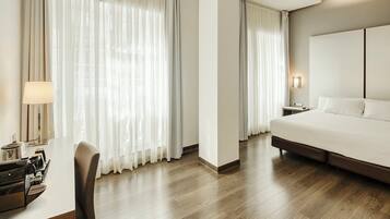 A hotel room with a bed, a desk with a lamp, and a chair.
