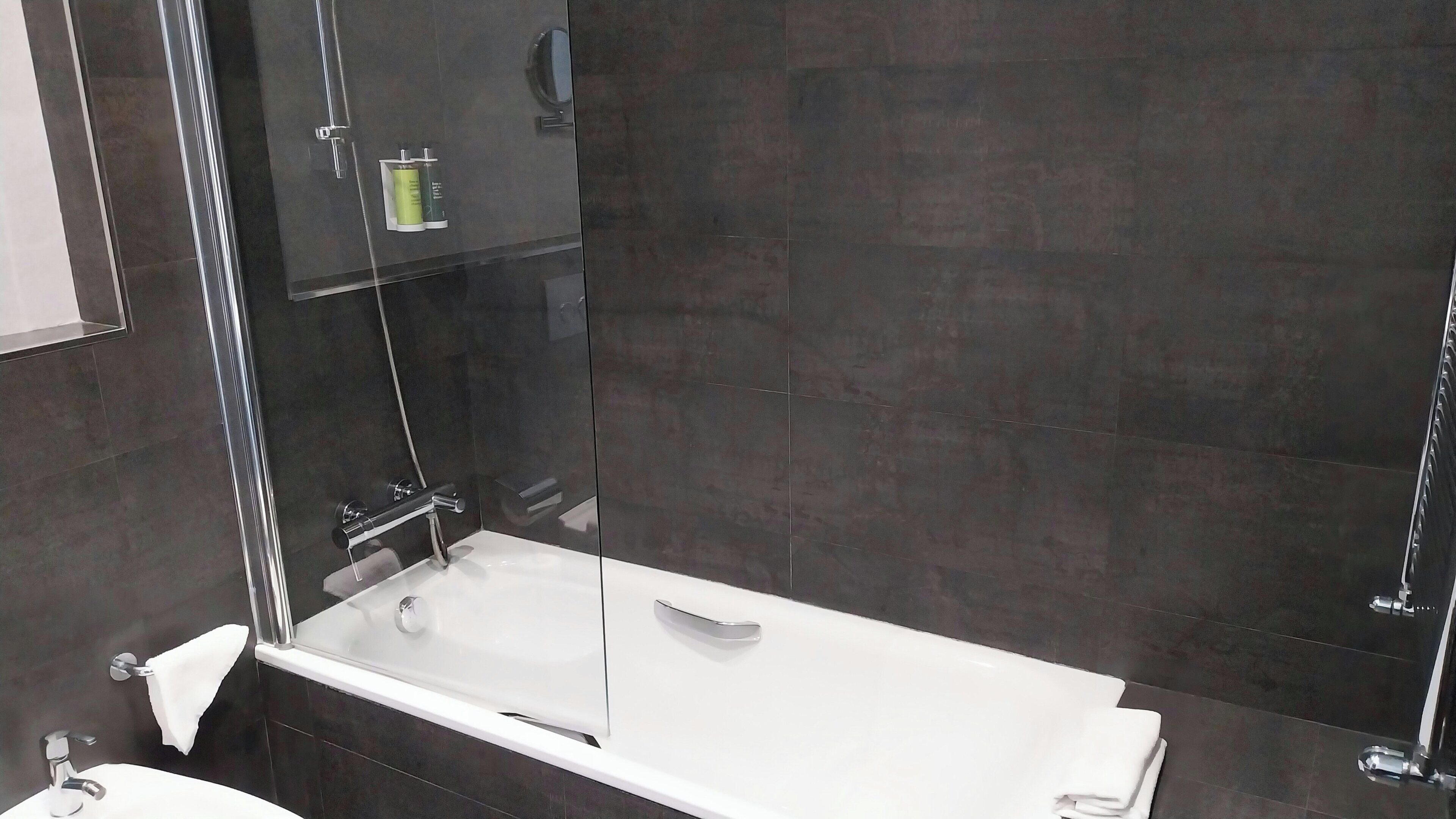 A modern bathroom with a glass-enclosed shower, a white bathtub, and a visible towel rack.