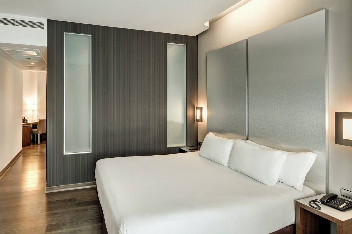 A hotel room with a large bed, a desk, a chair, a TV, and a door with a frosted glass panel.