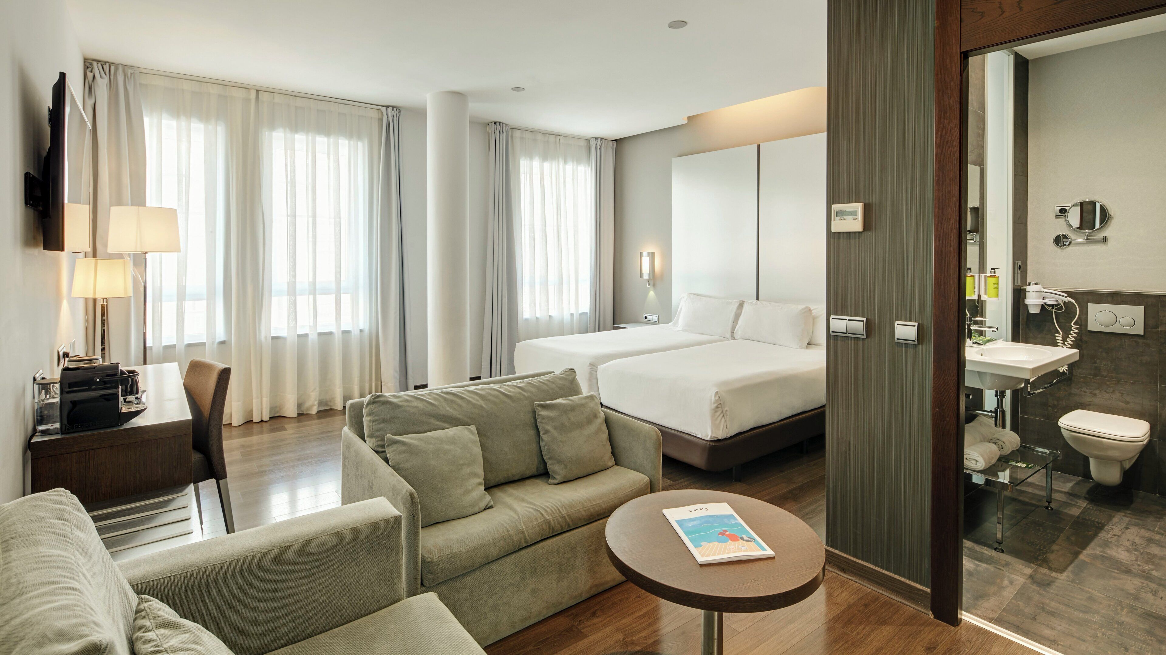 Una habitación de hotel con cama, sofá, escritorio, televisor y baño.