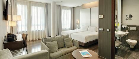 A hotel room with a bed, a sofa, a desk, a TV, and a bathroom.