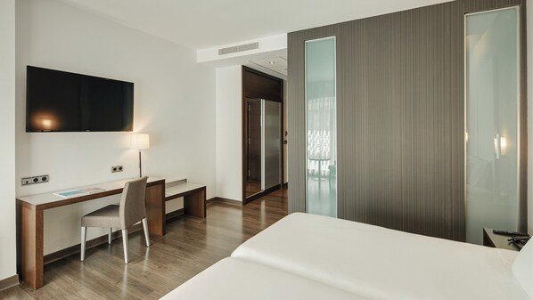A hotel room with a bed, desk, chair, TV, and a sliding door leading to a balcony.