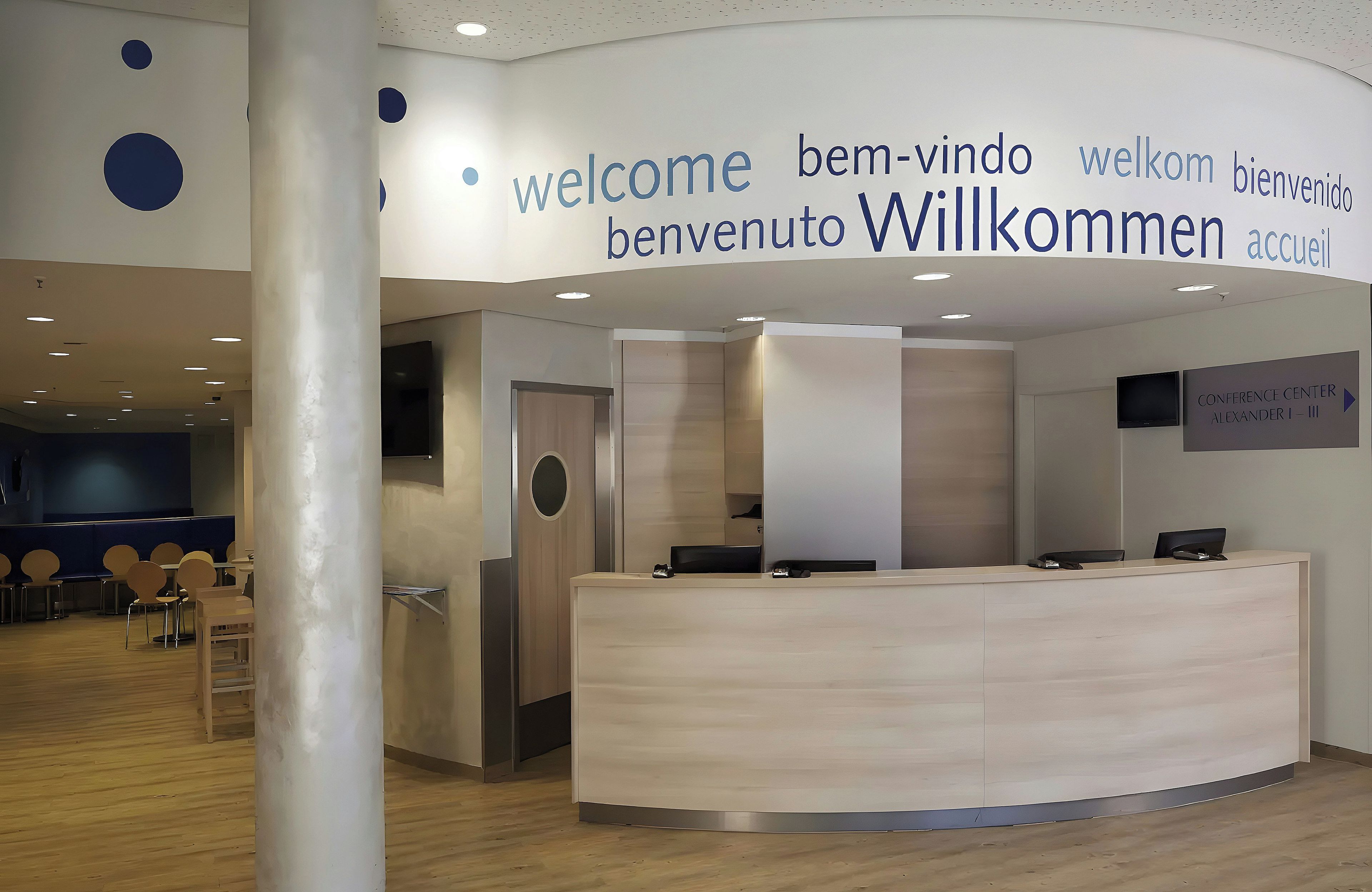 Ett modernt receptionsområde med ett centralt receptionsbord, en sittgrupp med stolar och en skylt med välkomstmeddelanden på flera språk.