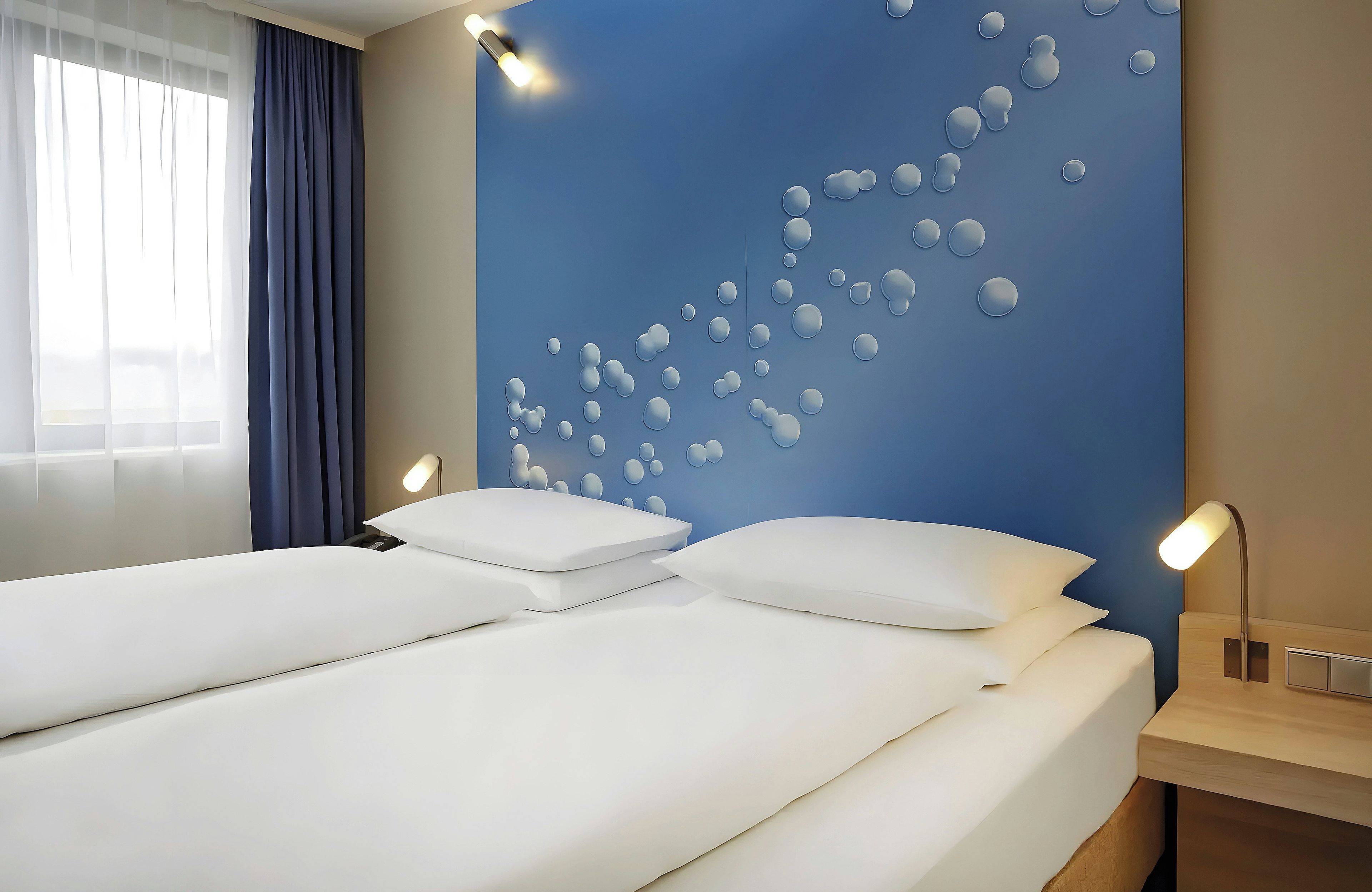 A hotel room with a large bed, a bedside table with a lamp, and a wall with a bubble pattern.
