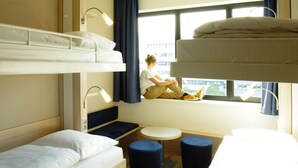 A compact hotel room with bunk beds, a small round table, and a window with a view of buildings. - Leonardo Smart Hotel Berlin Alexanderplatz (Berlin)