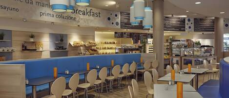 Café con menú de desayuno, asientos azules y una variedad de alimentos a la vista.