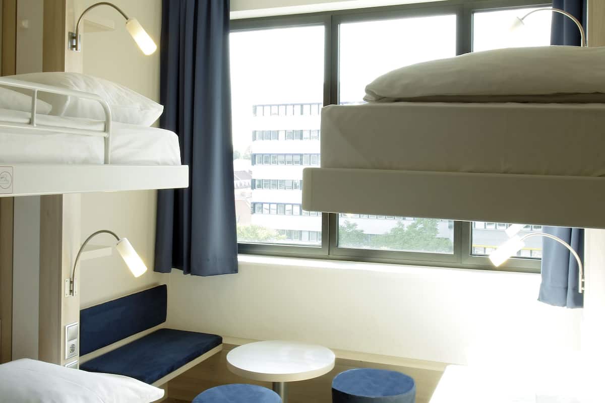 Dormitorio con literas, un escritorio, dos reposapiés y una ventana con cortinas.