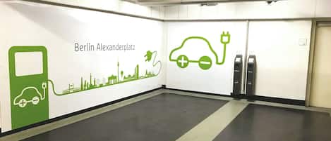 Zona de carga para vehículos eléctricos limpia y moderna, con un mural de paisaje urbano en la pared y señalización clara en el suelo.