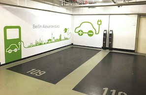 Zona de carga para vehículos eléctricos limpia y moderna, con un mural de paisaje urbano en la pared y señalización clara en el suelo.
