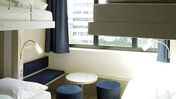 Ein kleines Hotelzimmer mit Stockbetten, einem kleinen Tisch und einem Fenster mit Blick auf Gebäude.