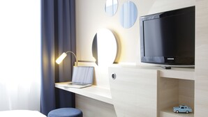 Ein Hotelzimmer mit einem Bett, einem Schreibtisch mit einem Laptop, einem Fernseher und einem kleinen Regal mit einem Spielzeugauto.