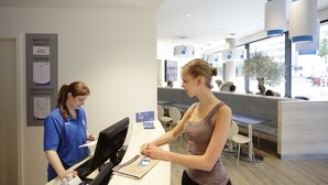 Ein Empfangsschalter mit Computer und einer ausgedruckten Karte, eine Sitzgelegenheit mit Tischen und Stühlen sowie ein Schwarzes Brett mit Aushängen.