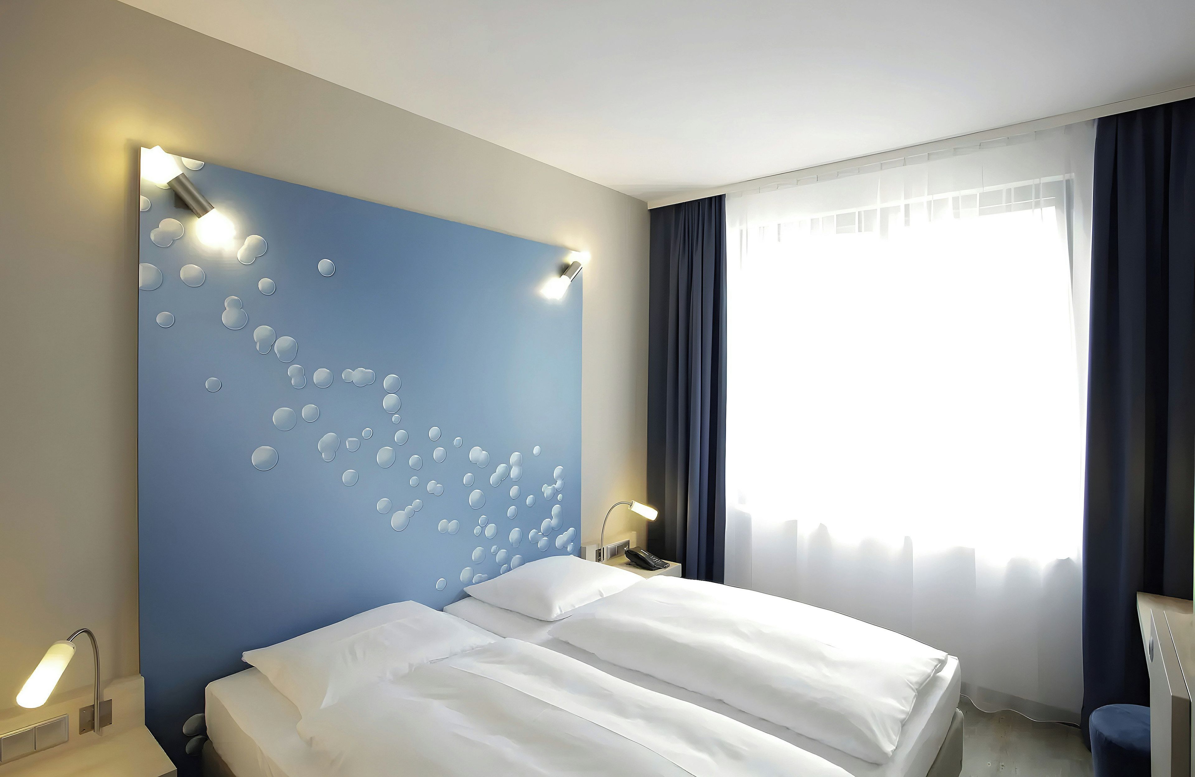 Ein Hotelzimmer mit einem Bett, einem Nachttisch mit Lampe, einer Wand mit Wabenmuster und einem Fenster mit Vorhängen.