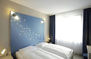 Habitación de hotel con cama, mesita de noche con lámpara, pared con diseño de burbujas y ventana con cortinas.