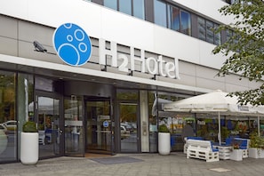 Welcome to H2 Hotel, featuring a modern exterior with a prominent logo, glass door, and outdoor seating area.