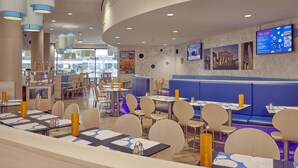 Ein modernes Restaurant mit runden Tischen, blauen Sitzbänken und einer digitalen Speisekarte.