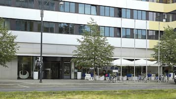 Un edificio moderno con fachada de vidrio, zona de estar al aire libre y un cartel de alquiler de bicicletas.