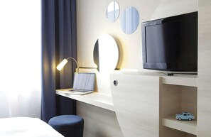 A modern hotel room with a desk, a laptop, a television, a bedside lamp, and a small toy car on a shelf. - Leonardo Smart Hotel Berlin Alexanderplatz (Berlin)