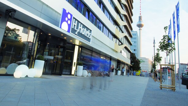 A modern hotel building with a prominent H Hotels sign, large windows, and a view of a tower in the background. - H2 Hotel Berlin Alexanderplatz (Berlin)