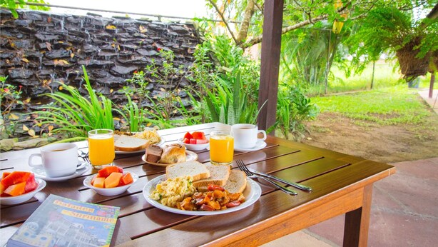 A breakfast table with plates of food, a cup of coffee, and a glass of orange juice. - Eco Torarica (Paramaribo)