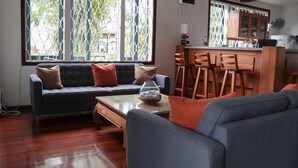 A living room with a sofa, a coffee table, and a dining area with wooden chairs and a kitchen counter. - Eco Torarica (Paramaribo)