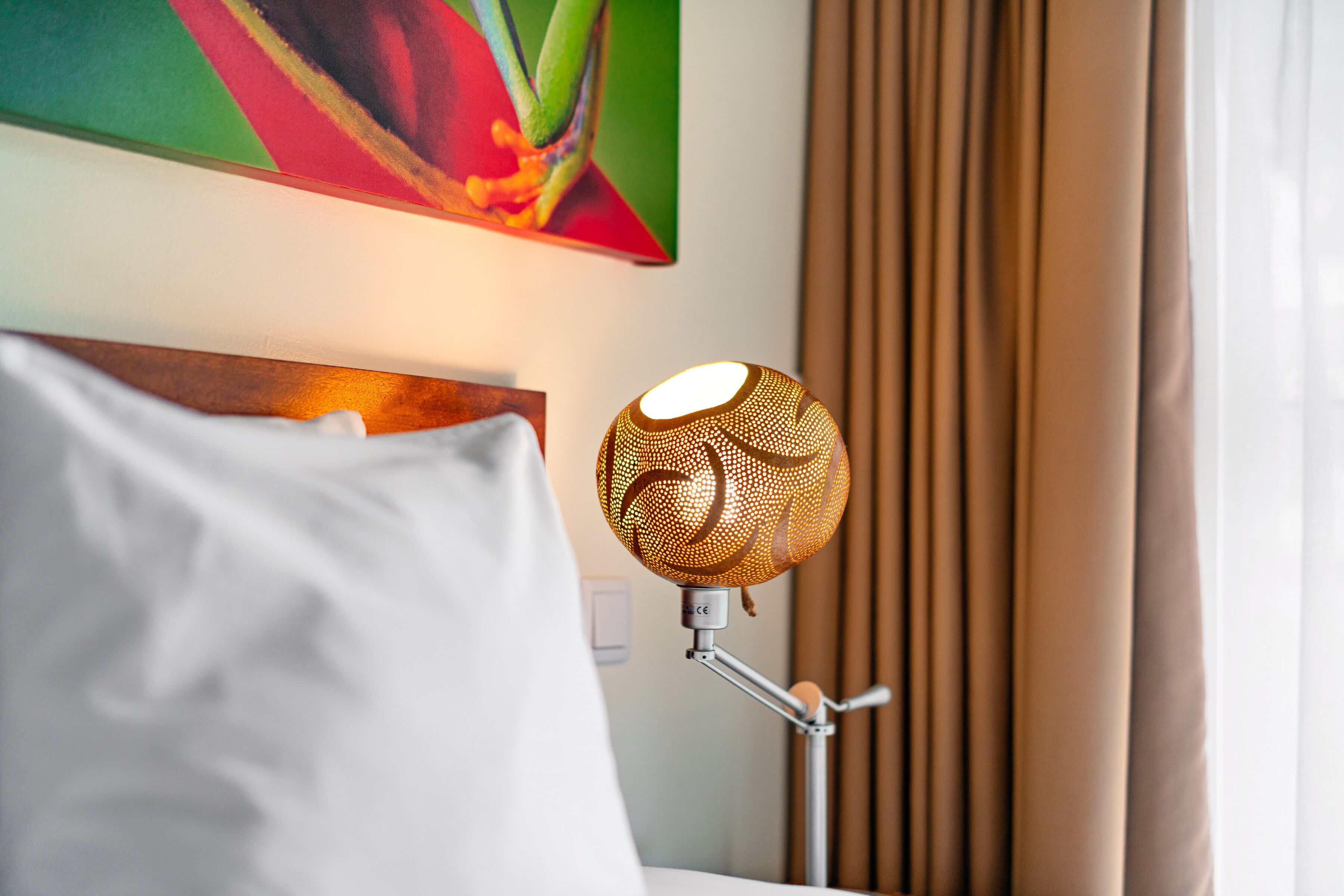 A hotel room with a bed, a wall-mounted lamp, and a painting above the bed.