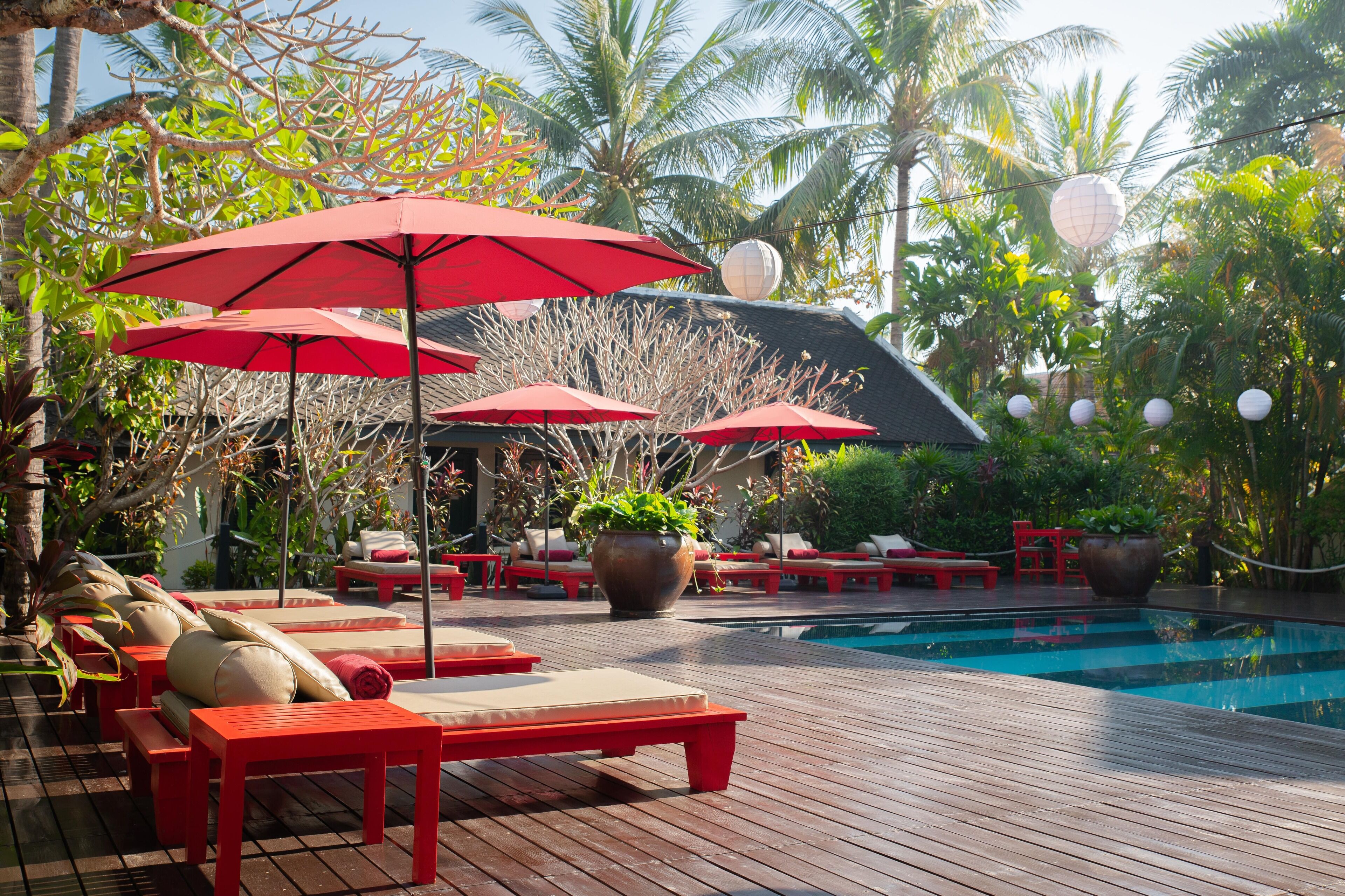 A poolside area with red umbrellas, lounge chairs, and potted plants.