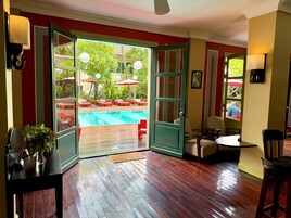 A room with a wooden floor, a pool visible through an open door, and outdoor seating with umbrellas.