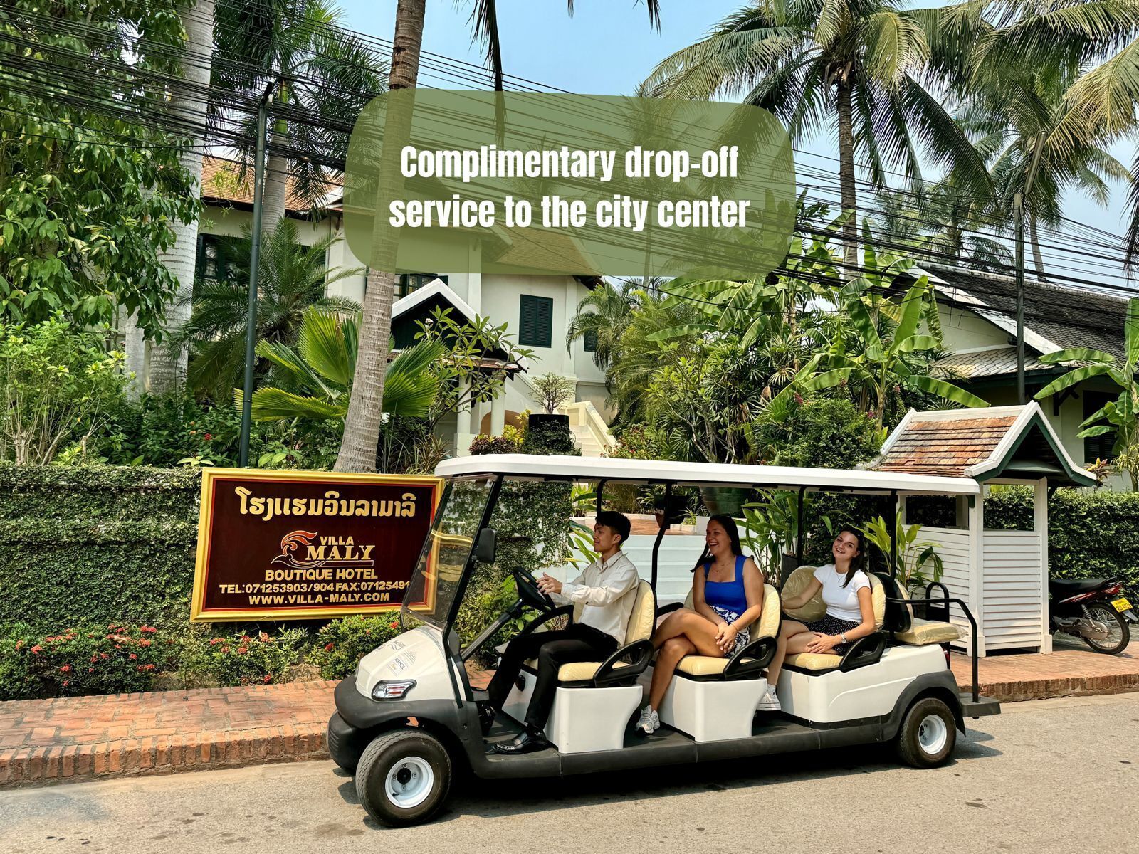 A golf cart with three passengers, parked in front of a hotel with a signboard.