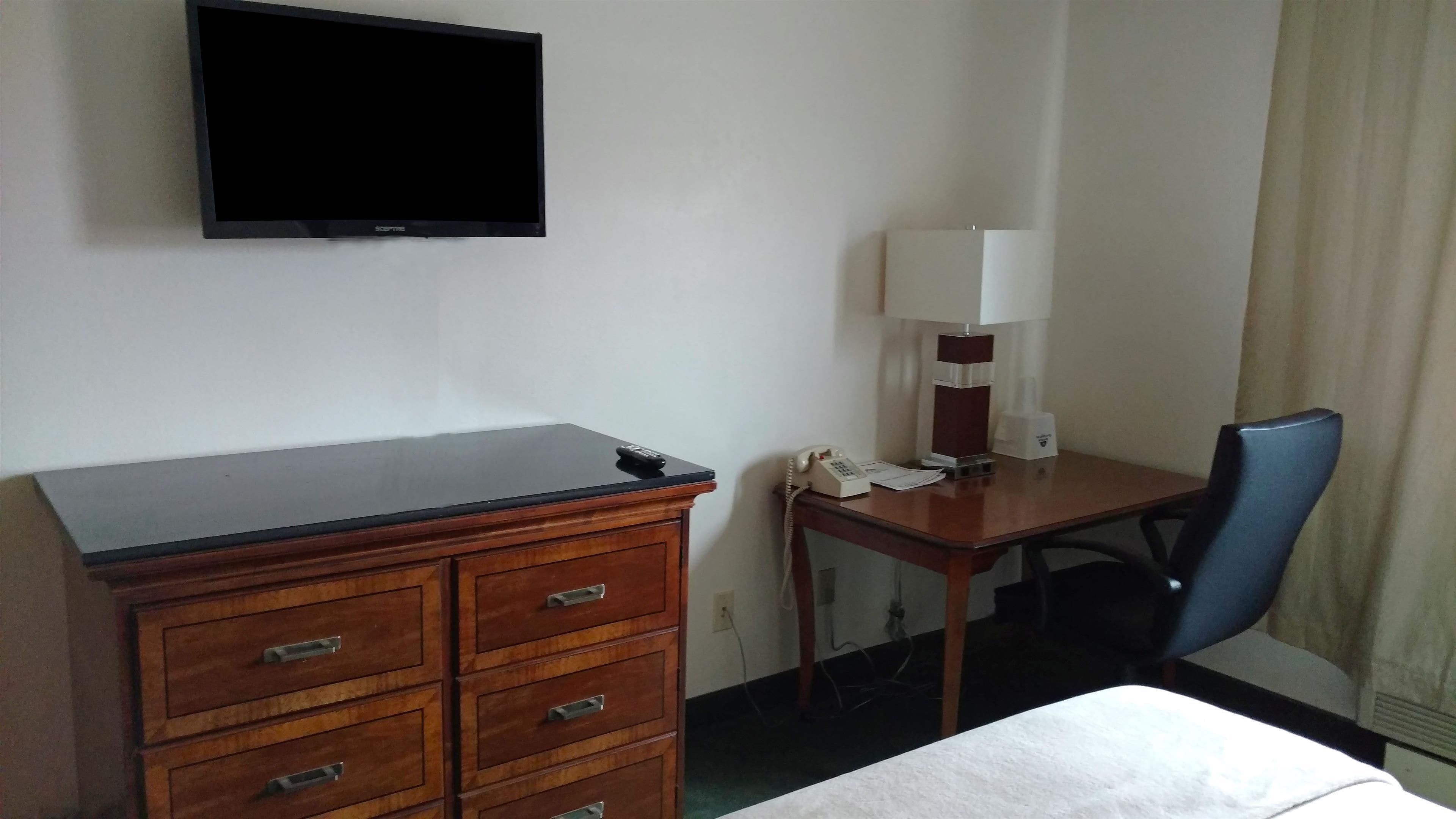Habitación de hotel con cómoda de madera, un escritorio con lámpara, teléfono y televisor montado en la pared.