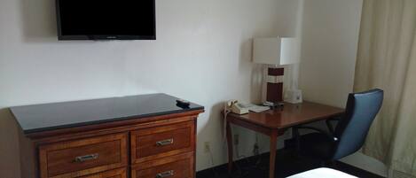 Habitación de hotel con cómoda de madera, un escritorio con lámpara, teléfono y televisor montado en la pared.