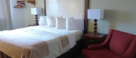 Habitación de hotel con una cama grande, dos mesitas de noche con lámparas, un sillón rojo y un cabecero de madera.