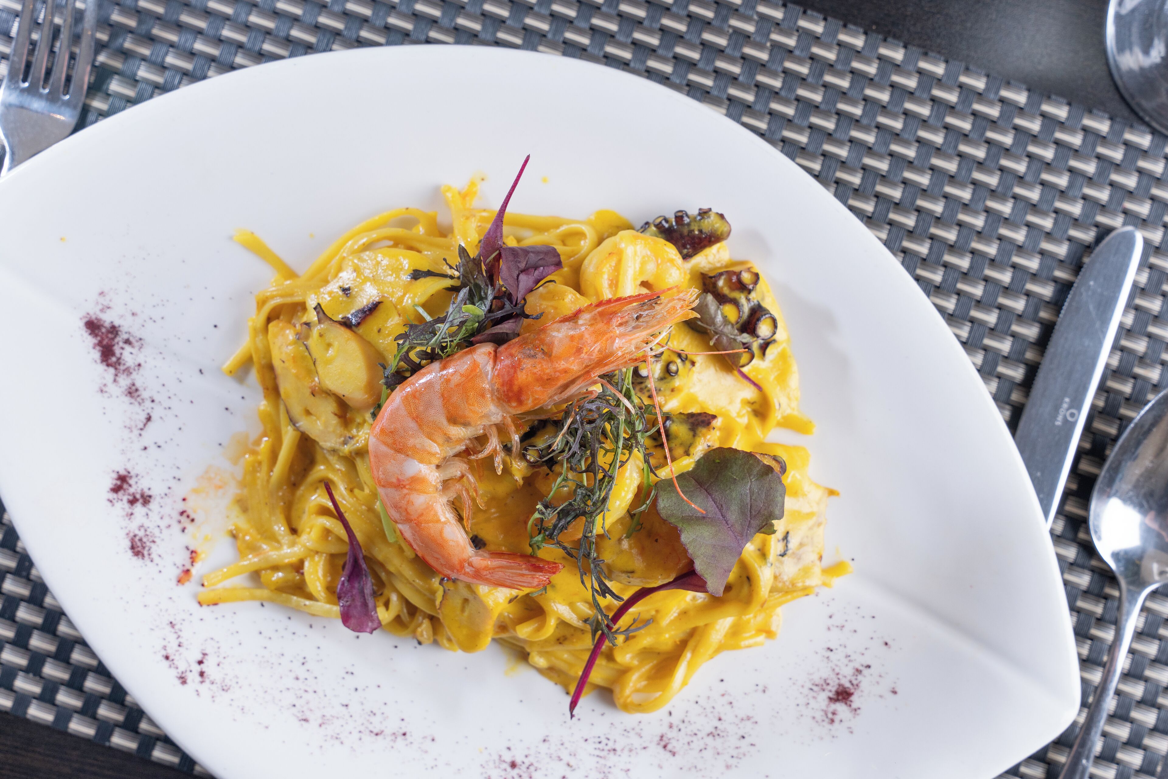 A plate of pasta with shrimp and greens on a white plate.