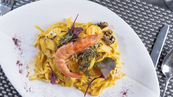 A plate of pasta with shrimp and greens on a white plate.