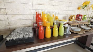 Mostrador de buffet con diversas bebidas coloridas en jarras y vasos, una selección de frutas y una exhibición de vasos vacíos.