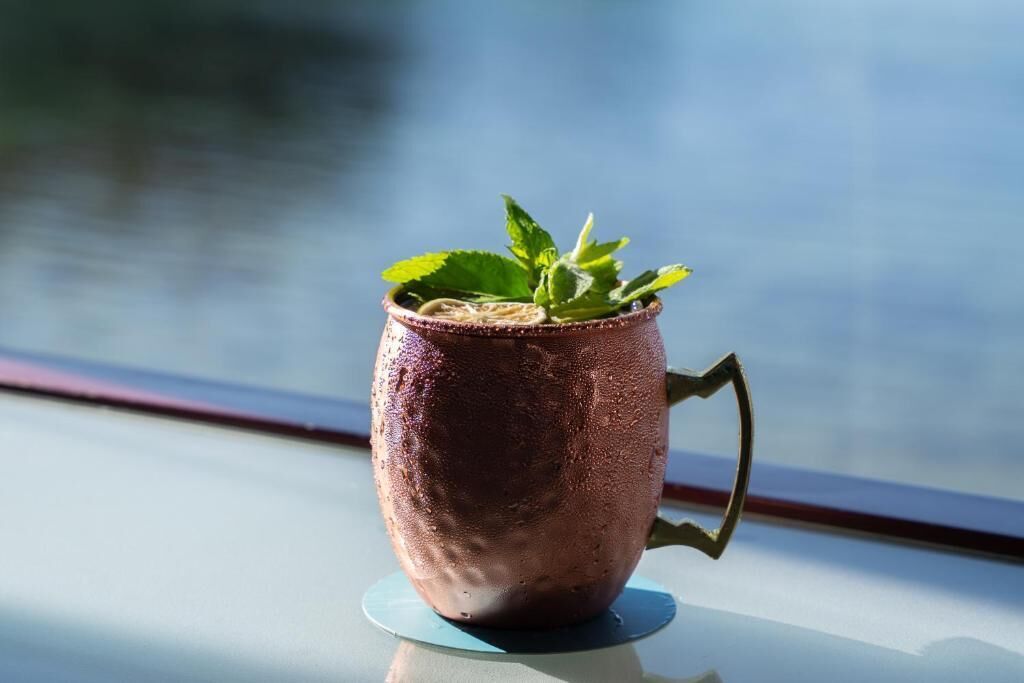 Une tasse en cuivre dotée d’une anse, posée sur une surface réfléchissante.