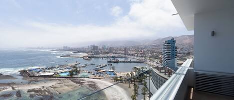 Ein Balkon mit Blick auf eine Küstenstadt, darunter ein Strand, ein Yachthafen und Gebäude.