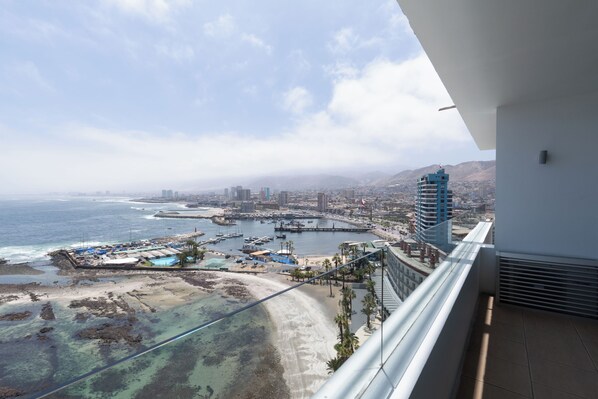 Un balcón con vista a una ciudad costera, que incluye una playa, un puerto deportivo y edificios.