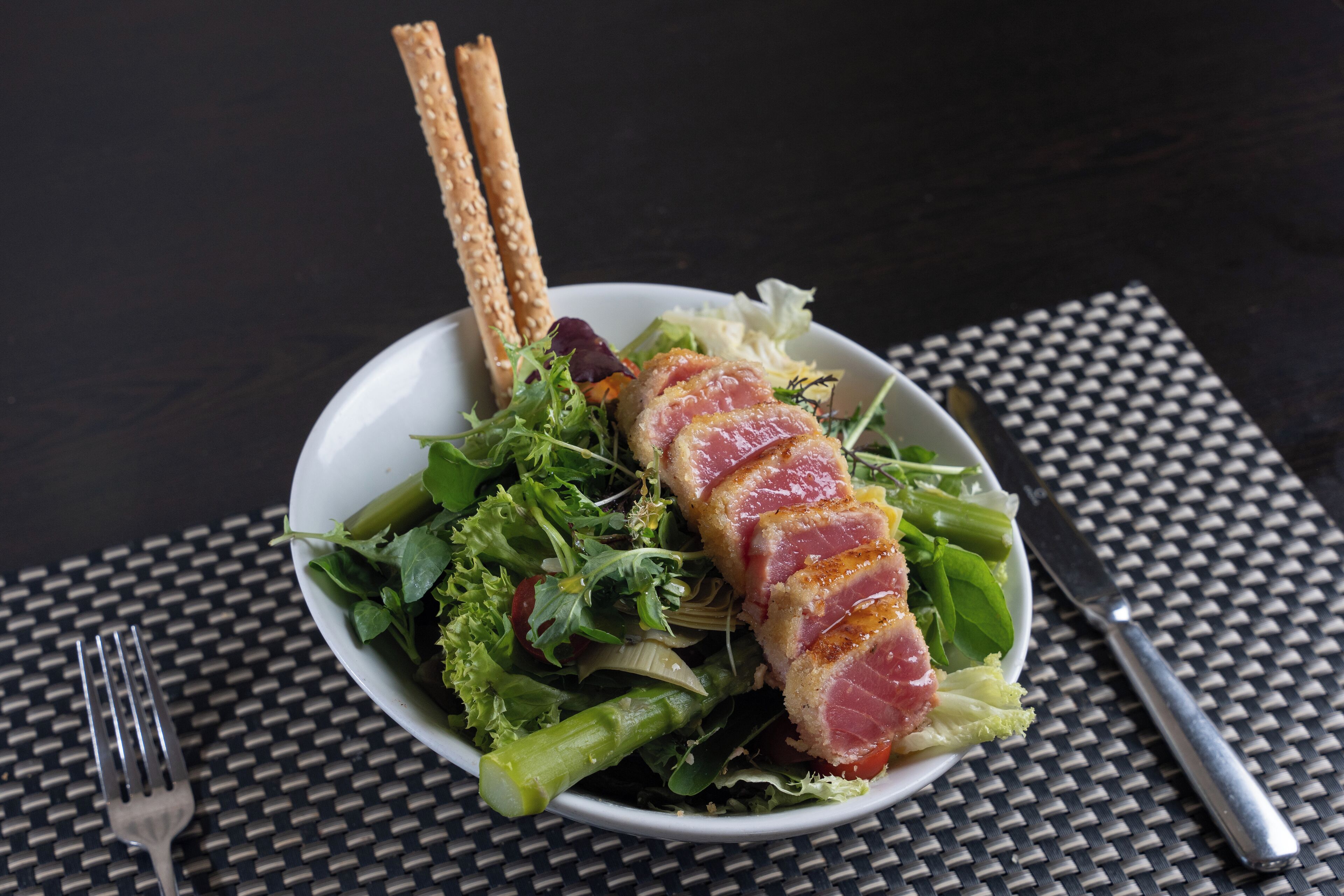 A plate of food with a piece of meat, greens, and crackers on a dark table.