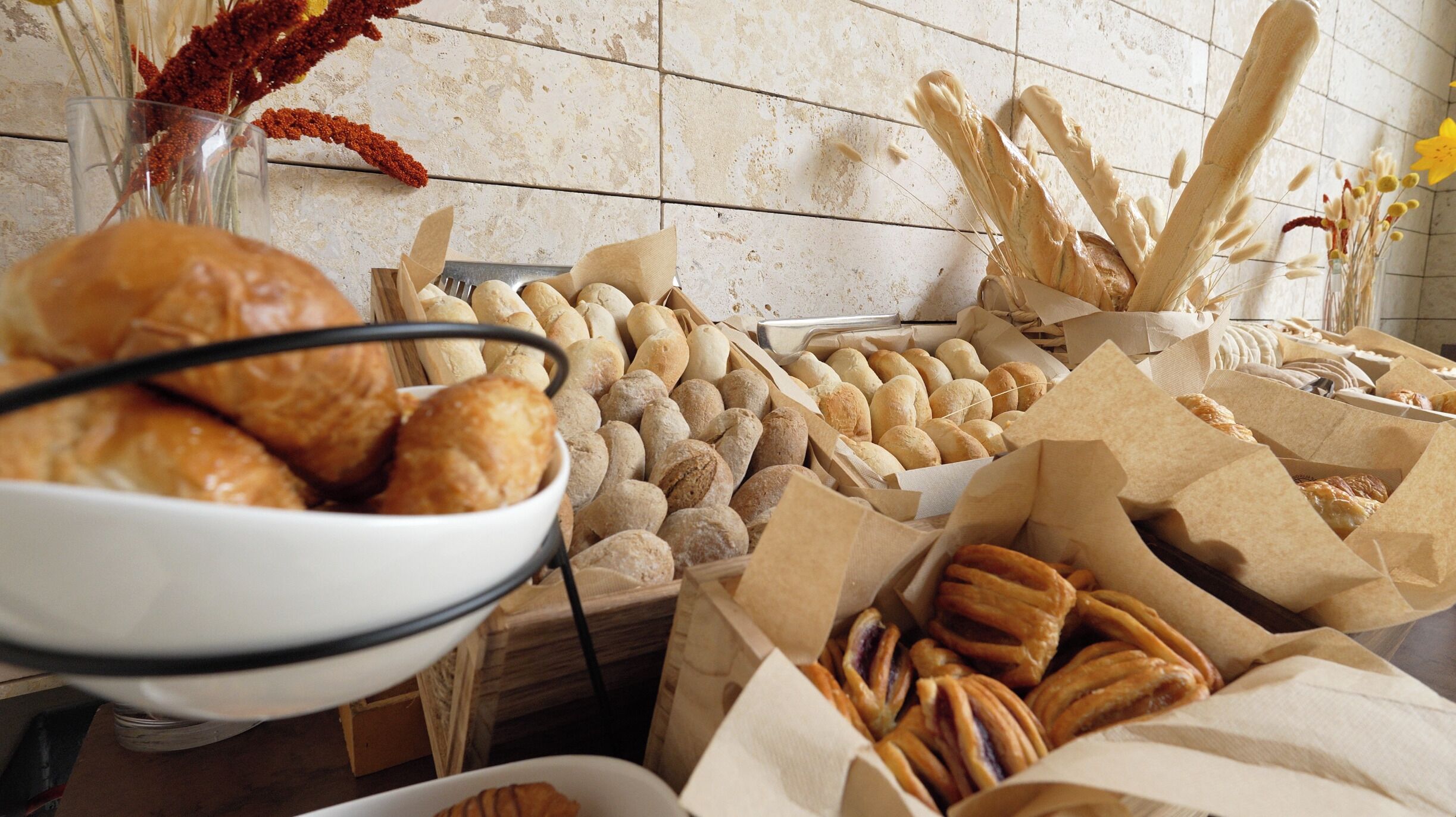 Une variété de produits de boulangerie présentés dans des paniers et des bols, ce qui évoque l’ambiance d’une boulangerie ou d’un café.
