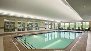 An indoor swimming pool with clear water, surrounded by a tiled floor and a glass wall.