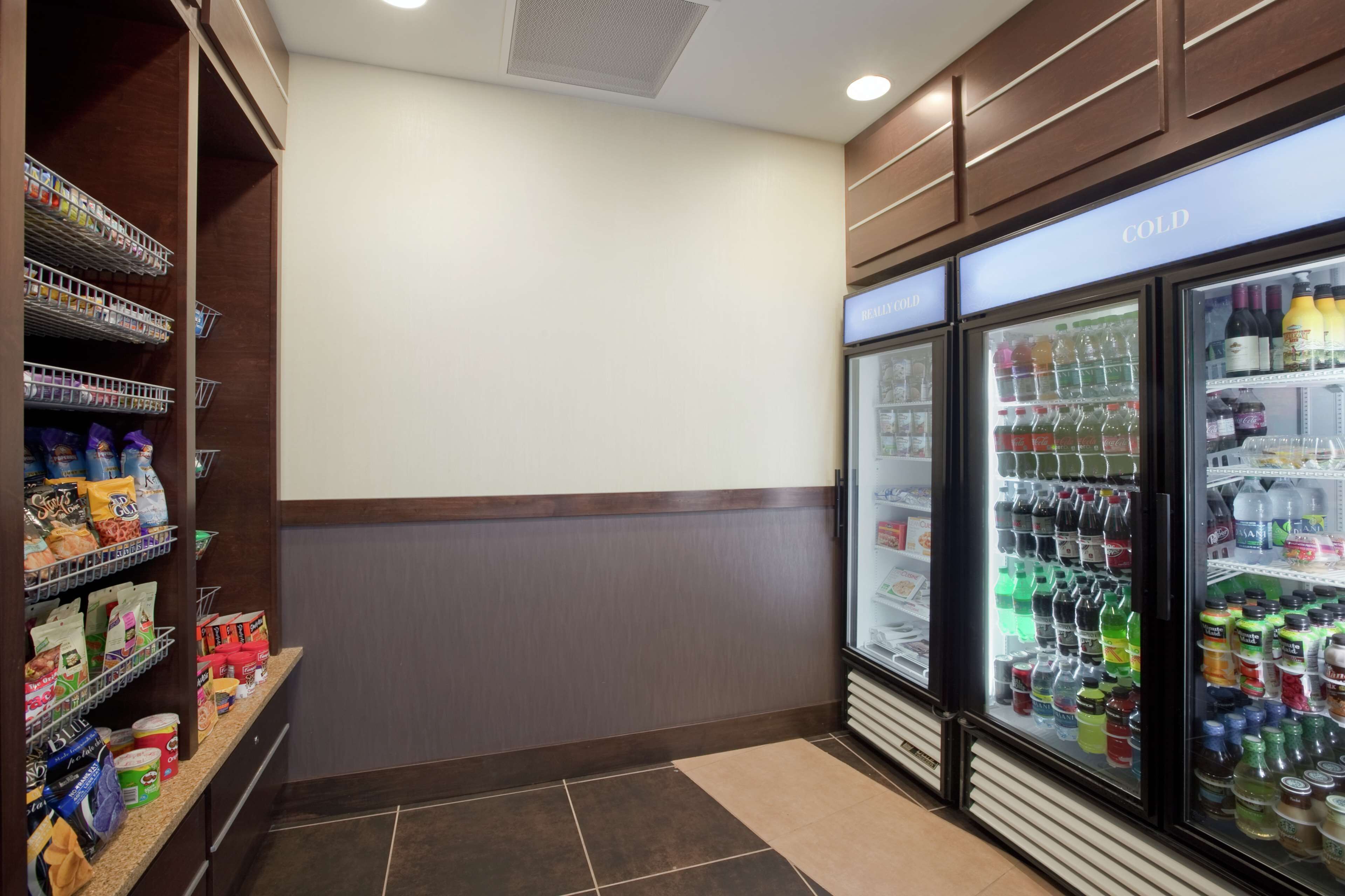 A corner of a hotel room with a minibar, a refrigerator stocked with beverages, and a shelf with snacks.
