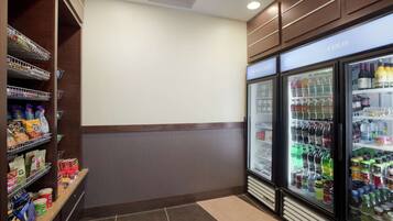 A corner of a hotel room with a minibar, a refrigerator stocked with beverages, and a shelf with snacks.