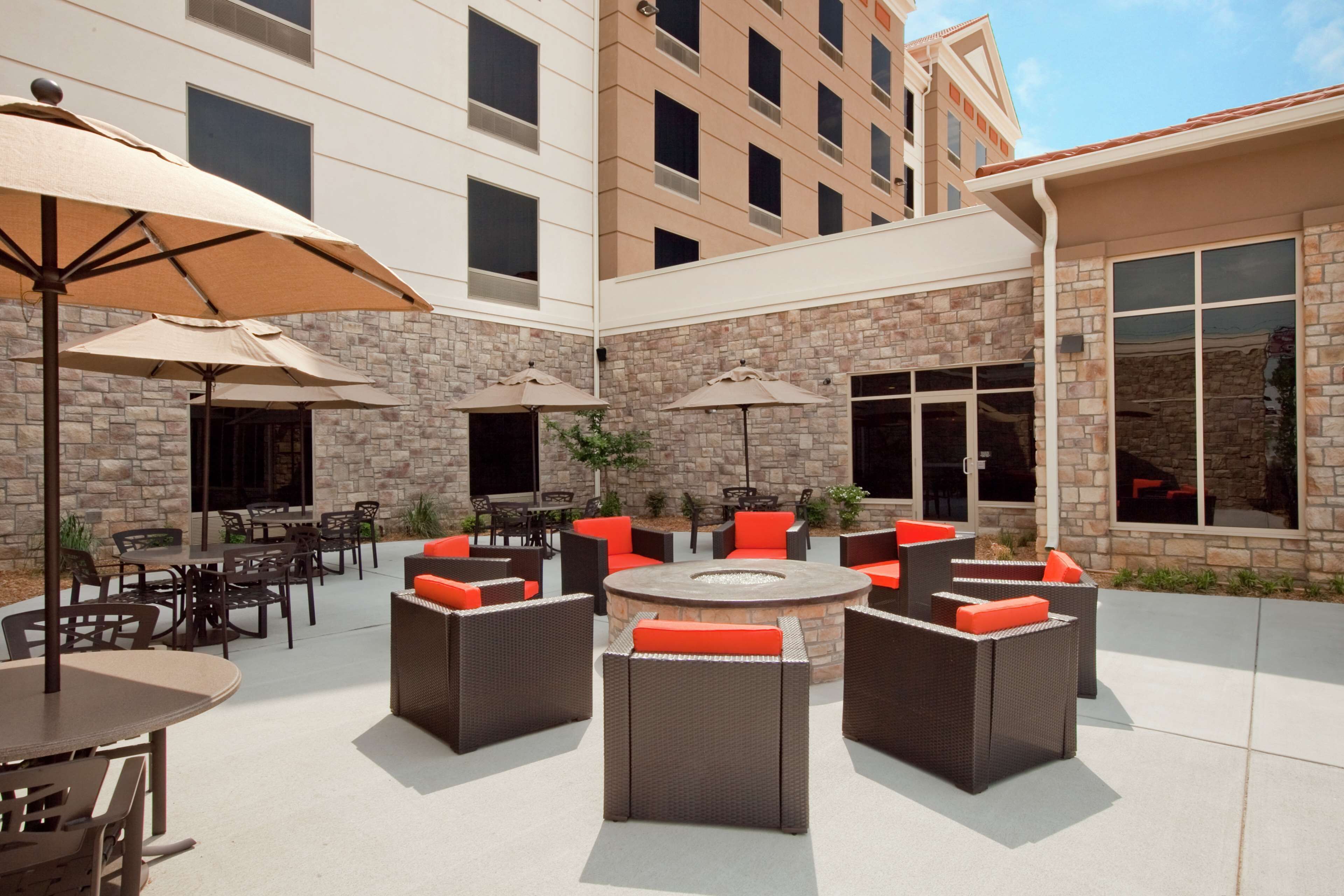 An outdoor patio area with multiple tables and chairs, surrounded by stone walls and large windows.