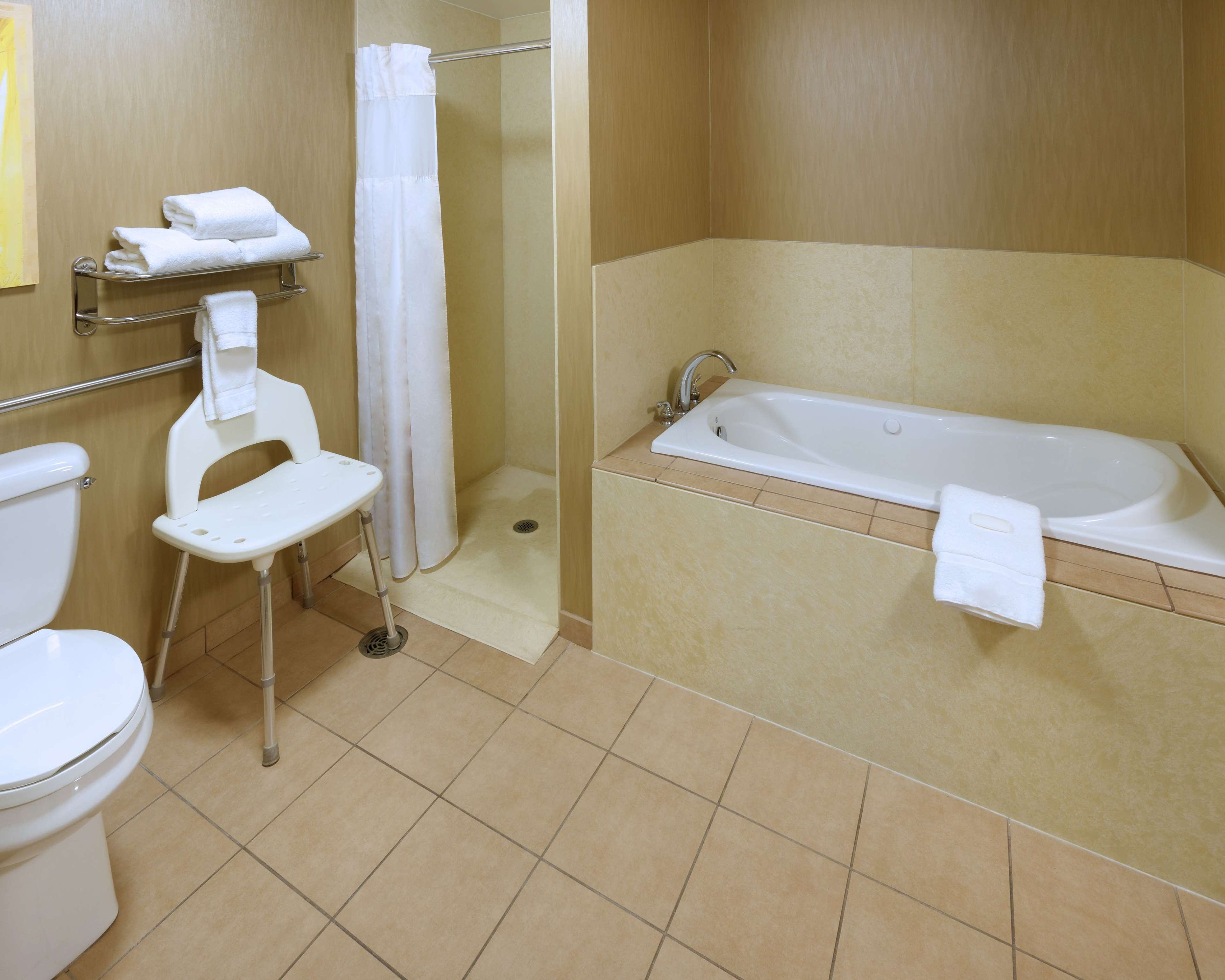 Un baño con inodoro, ducha con puerta de cristal, bañera y una pequeña silla blanca.