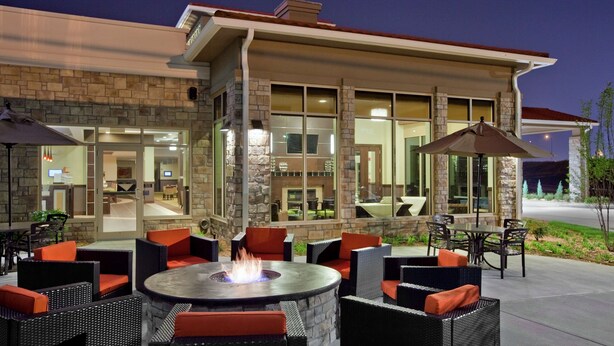 An outdoor patio area with wicker furniture, a central fire pit, and large windows.