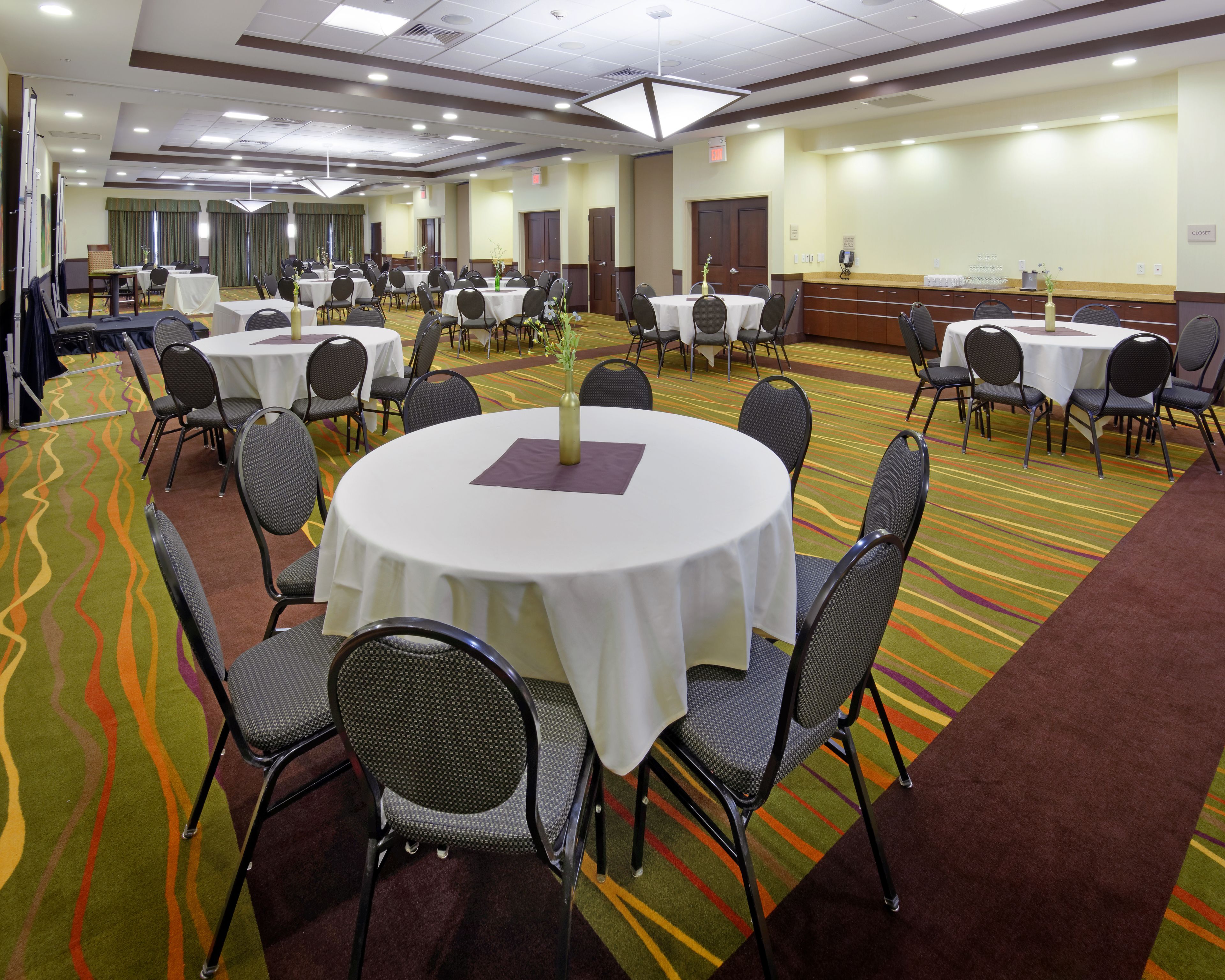 A conference room with multiple round tables, each surrounded by chairs, and a carpeted floor with a wavy pattern.