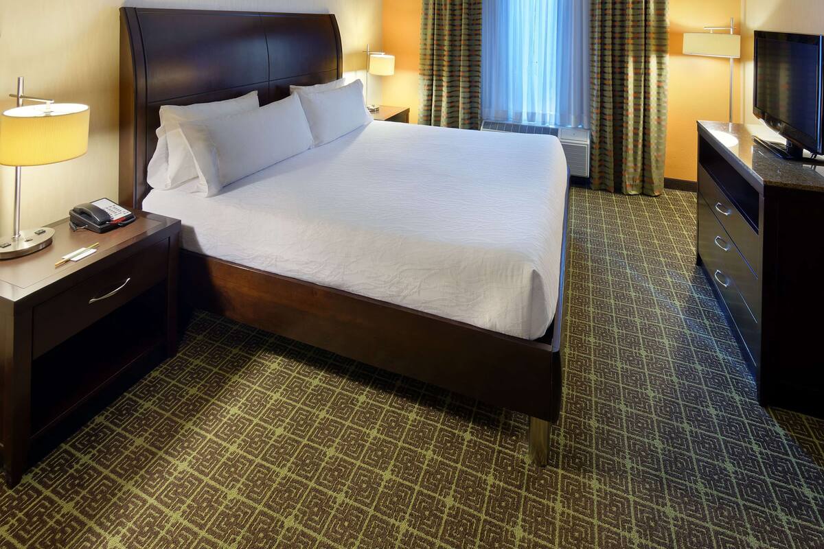 A hotel room with a large bed, a bedside table with a lamp, a telephone, and a television.
