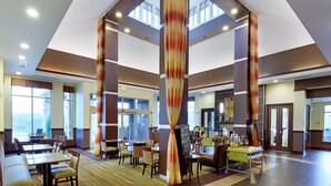 A spacious hotel lobby with high ceilings, large windows, and a central seating area with tables and chairs.